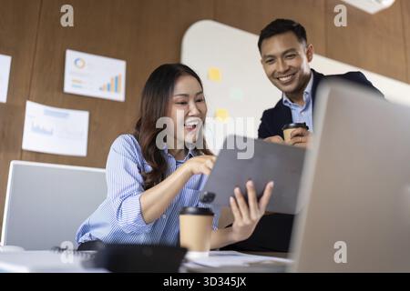 A business team collaborates enthusiastically over a digital tablet in a modern office, reflecting teamwork and innovation Stock Photo