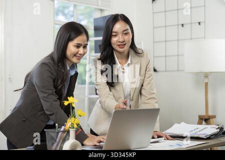 Two women in business attire collaborating on project details, sharing ideas, and analyzing data in a modern office setting Stock Photo