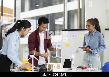 A diverse group of engineers collaborates on a sustainable energy project, showcasing wind turbines and eco-friendly designs in a bright office space Stock Photo