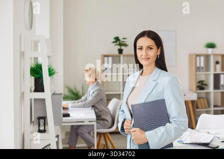 Successful woman in elegant clothing holding notepad and posing in office room finished work in time Stock Photo