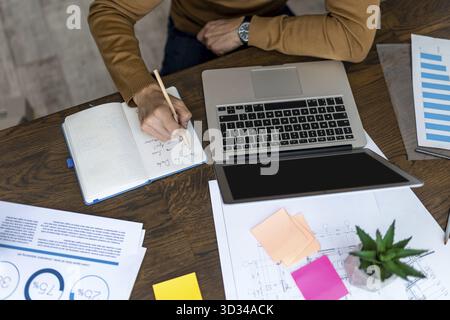 Unrecognizable male use laptop writing down important data in notebook, working on computer or studying online noting information, making notes Stock Photo