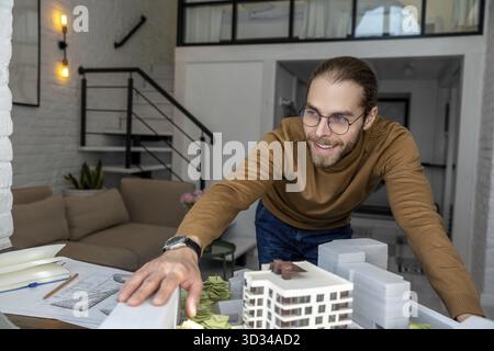 Smiling man architect in glasses working in office with on creation of new residential complex, designing layout of buildings Stock Photo