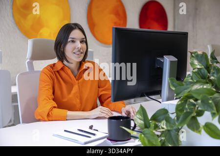 Concentrated young Caucasian female office worker seated at the desk looking at the computer monitor Stock Photo