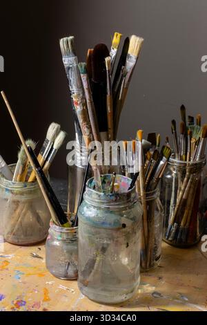 Assortment of Paintbrushes in Glass Jars on an Artist’s Work Table Stock Photo