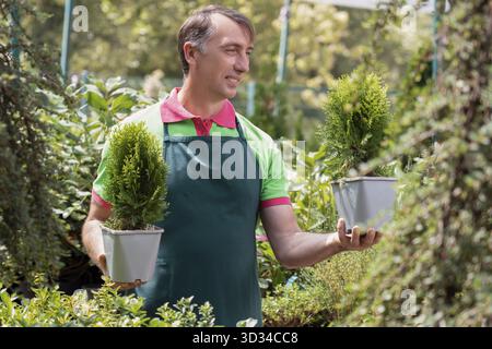 Man working in garden center standing and holding plants Stock Photo