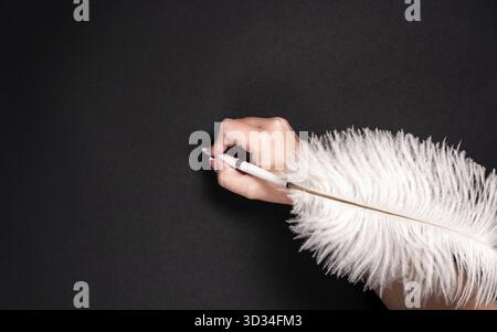 Female hand holding feather pen over black background Stock Photo