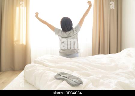 Sleeping mask on a bed with stretching woman in the background, back view Stock Photo