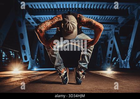 Young cool man break dancer posing on urban bridge at night, tattoo on body Stock Photo