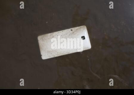 Mobile phone lying on pavement in puddle Stock Photo