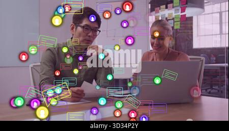 Two professionals collaborating at office table, reviewing report with laptop and digital icons Stock Photo