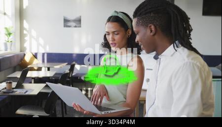 Collaborating colleagues examining laptop projecting green hologram icon in lounge with coffee cup Stock Photo