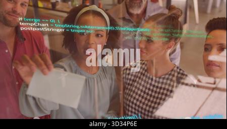 Collaborating team placing index cards on transparent board at open-plan office, with code snippets Stock Photo