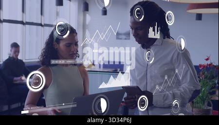 Coworkers collaborating on laptop and tablet in office wearing office attire, with digital graphs Stock Photo