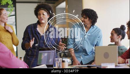Gesturing woman presenting digital infographic overlay at meeting room with laptops Stock Photo