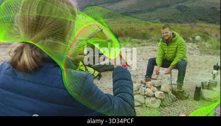 Man in green jacket roasting marshmallows over campfire at campsite with neon mesh, copy space Stock Photo