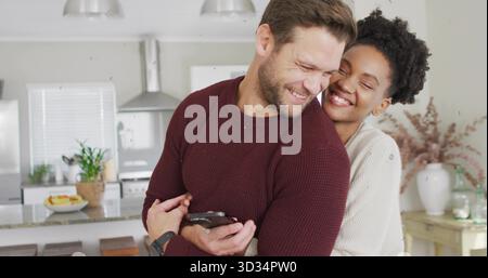Hugging couple sharing warm embrace in bright modern kitchen, with smartphone and marble countertop Stock Photo