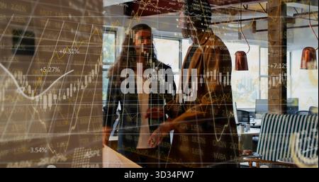 Discussing two professionals in blazers analyzing stock data in lounge with overlaid stock charts Stock Photo