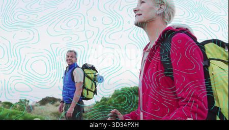 Trekking couple wearing outdoor gear along grassy coastal trail, with backpacks and trekking pole Stock Photo