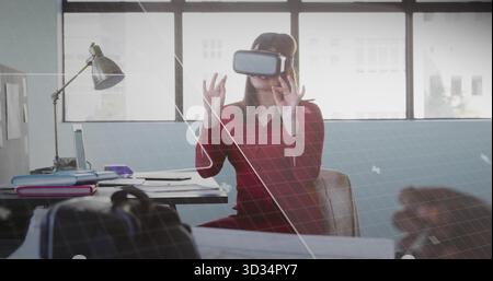 Reaching out worker wearing red dress VR headset at office, engaging VR interface with laptop Stock Photo