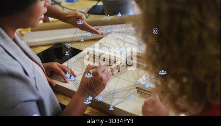 Collaborating designers wearing blazers sketching wooden scale model in studio, with overlay icons Stock Photo