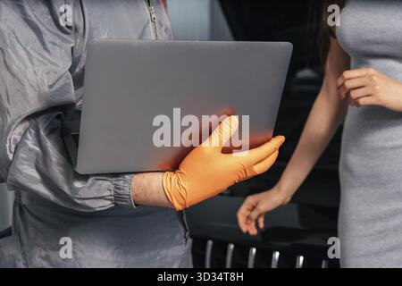 Car mechanic communicating with a customer while using laptop and examining vehicle breakdown at auto repair shop Stock Photo