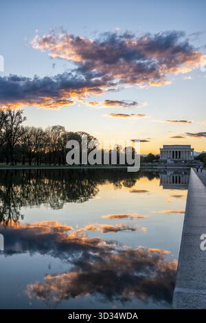Lincoln Memorial Reflecting Pool At Sunset Washington DC // WASHINGTON DC — The Lincoln Memorial Reflecting Pool at sunset reflects clouds. This iconic pool is a prominent feature of the National Mall, stretching approximately 618 meters (2,029 feet) long and 51 meters (167 feet) wide. The Lincoln Memorial, a neoclassical temple honoring Abraham Lincoln, is situated at its western end. Dedicated in 1922, the memorial and pool are significant national landmarks. They are popular tourist destinations in Washington D.C. Stock Photo