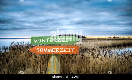 An image with a signpost pointing in two different directions in German. One direction shows Daylight Saving Time, the other shows Winter Time. Stock Photo