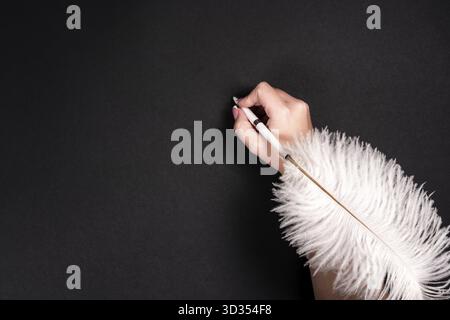 Female hand holding feather pen over black background Stock Photo