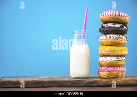 Milk bottle and stack of donuts on wooden board, negative space bright background Stock Photo