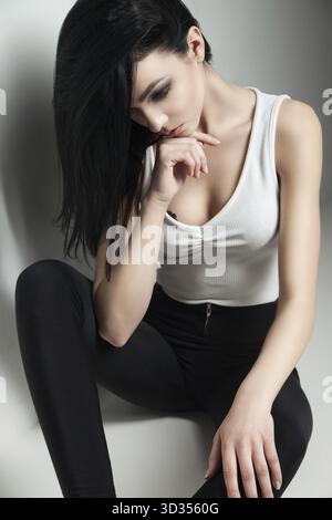 Cloe-up of black-haired model with make-up sitting on floor and looking up.Studio shot Stock Photo
