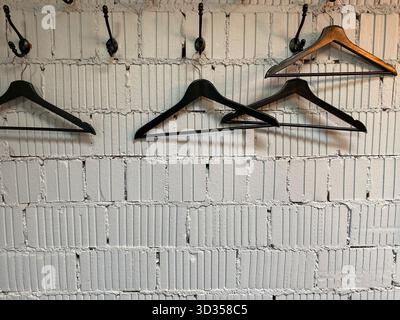 Empty hangers on rustic white brick wall, creating a minimalist and industrial background. Mobile photo Stock Photo