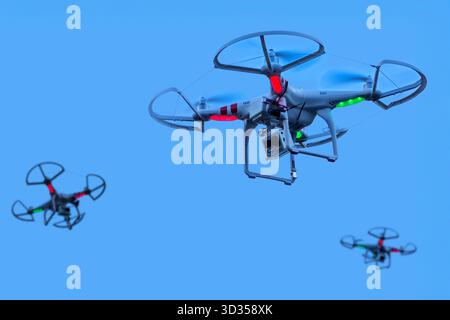 Three miniature quadcopter drones / teleoperated unmanned aerial vehicles / UAV equipped with cameras for aerial photography in flight in group Stock Photo