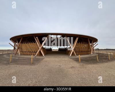 Timber amphitheatre with sweeping wooden roof and tiered seating on an indigenous reserve, set against vast prairies, symbolizing sustainable design. Stock Photo
