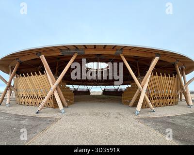 Timber amphitheatre with sweeping wooden roof and tiered seating on an indigenous reserve, set against vast prairies, symbolizing sustainable design. Stock Photo