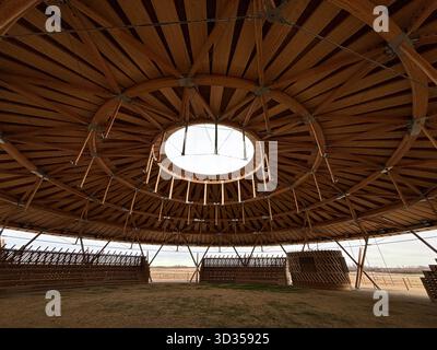 Timber amphitheatre with sweeping wooden roof and tiered seating on an indigenous reserve, set against vast prairies, symbolizing sustainable design. Stock Photo