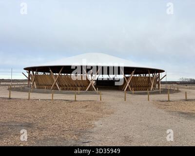 Timber amphitheatre with sweeping wooden roof and tiered seating on an indigenous reserve, set against vast prairies, symbolizing sustainable design. Stock Photo