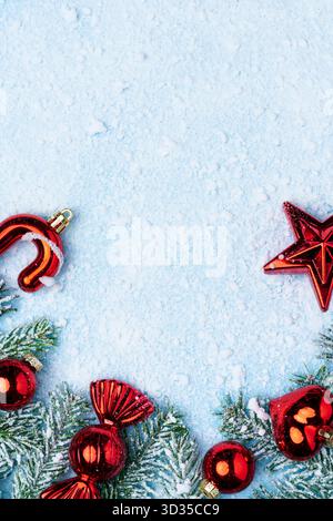 Festive Christmas composition with red ornaments, candy cane, and frosted fir branches on light blue snowy background. Stock Photo