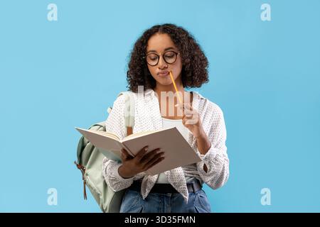 Thoughtful African American Student Engaged in Reading and Studying at a Blue Studio Backdrop Stock Photo