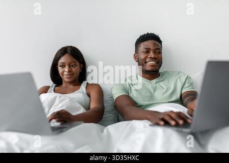Couple Working on Laptops While Relaxing in Bed During a Cozy Indoor Evening Stock Photo