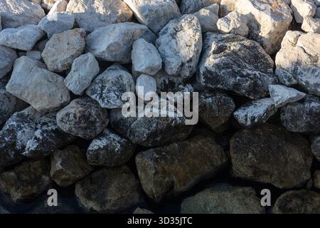 A dense collection of rough, weathered rocks forms a natural stone wall texture. Perfect for outdoor design, landscaping, or background imagery emphas Stock Photo