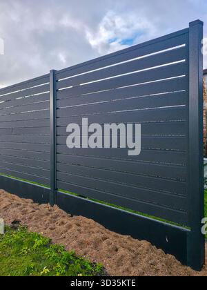 New modern dark gray metal fence with raindrops on panels and cloudy sky background Stock Photo