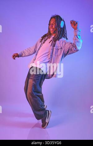 Young man enjoying music with headphones while dancing in neon light Stock Photo