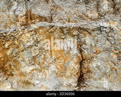 Close-up of a rugged rock surface showing natural mineral layers and textures in shades of gray, brown, and gold, revealing geological formations. Stock Photo