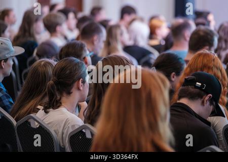 Attendees sit in rows in conference room, focused on stage, diverse group, casual attire, engaged audience, moments of concentration and quiet anticipation during talks and presentations Stock Photo