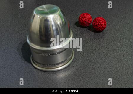 Scene24-Shot1-Close-up of an inverted metallic cup and two handmade red knitted balls on a gray textured surface. Perfect for minimalist composition, Stock Photo