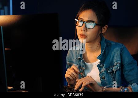 Portrait young beautiful Asian creative with glasses of serious face looking on pc to search project creator social media online, planning strategy Stock Photo