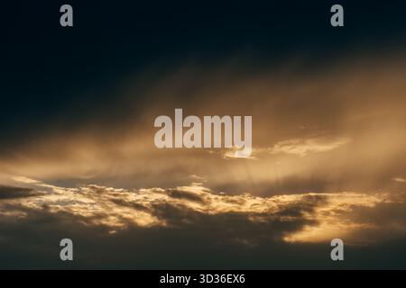 A glowing golden sunset illuminates layered clouds with soft shadows, capturing the serenity and beauty of an evening sky. Stock Photo
