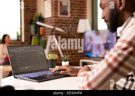 Closeup of black man typing HTML code on laptop keyboard, working remotely from desk. African american developer writing website code and running software scripts for tech company project at home. Stock Photo