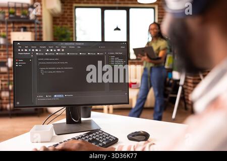 African american software developer typing at home desk, refining code and solving bugs on computer. Male remote worker focuses on improving application performance in home workstation. Stock Photo