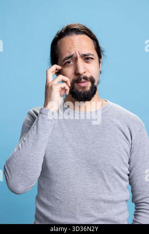 Middle eastern uncertain person feeling unsure and confused against blue background, contemplating and feeling curious in studio. Young adult acting thoughtful and reflective, decision making. Stock Photo